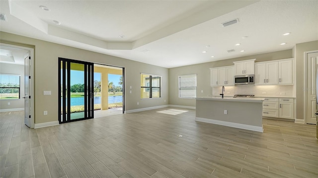 kitchen with white cabinetry, a tray ceiling, a center island with sink, and a water view