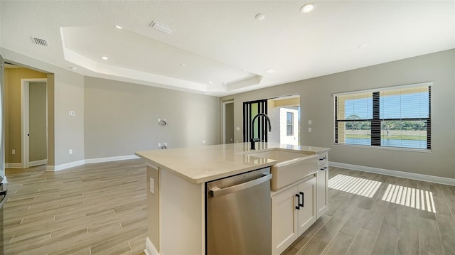 kitchen featuring a tray ceiling, white cabinets, stainless steel dishwasher, and a kitchen island with sink