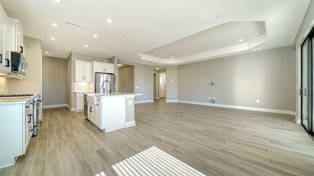 kitchen featuring an island with sink, a tray ceiling, stainless steel appliances, and white cabinetry