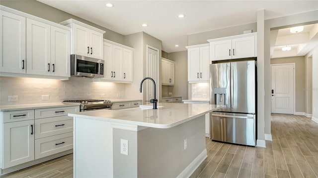 kitchen featuring white cabinets, appliances with stainless steel finishes, an island with sink, sink, and backsplash