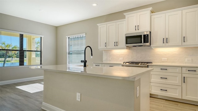 kitchen with sink, white cabinetry, light hardwood / wood-style flooring, an island with sink, and stainless steel appliances