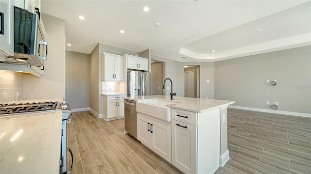 kitchen with white cabinets, appliances with stainless steel finishes, backsplash, light stone counters, and a center island with sink