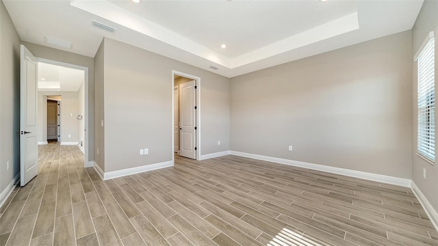 empty room featuring light wood-type flooring and a raised ceiling