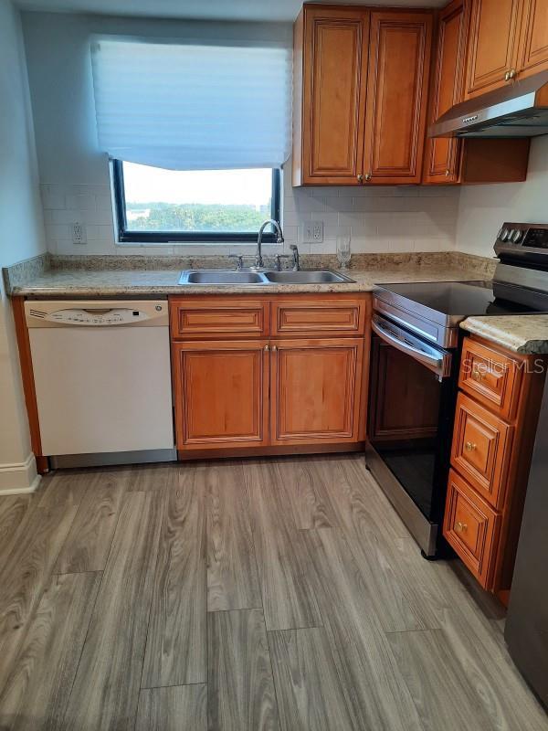 kitchen featuring stainless steel electric stove, light wood-type flooring, sink, and white dishwasher