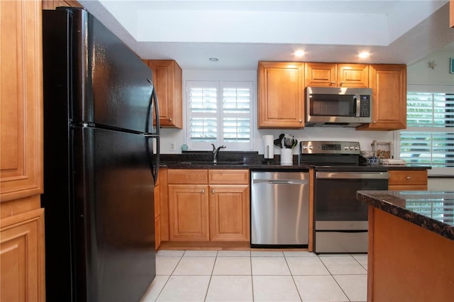 kitchen with sink, dark stone countertops, light tile patterned floors, stainless steel appliances, and plenty of natural light