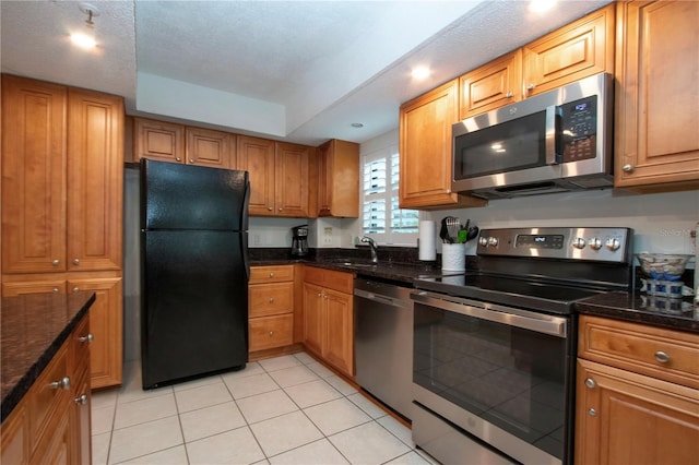 kitchen featuring stainless steel appliances, a tray ceiling, sink, and dark stone countertops