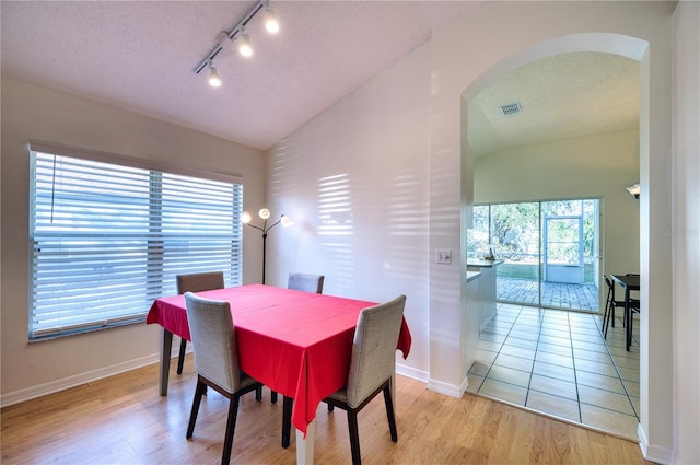 dining space with lofted ceiling, light hardwood / wood-style floors, and a textured ceiling