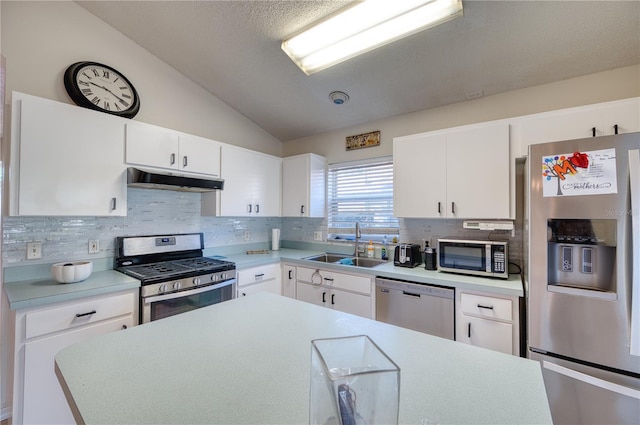 kitchen with lofted ceiling, sink, appliances with stainless steel finishes, white cabinetry, and tasteful backsplash