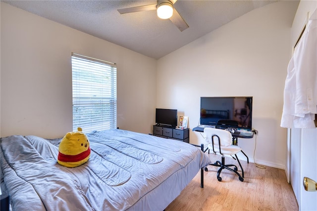 bedroom with a textured ceiling, vaulted ceiling, ceiling fan, and light wood-type flooring