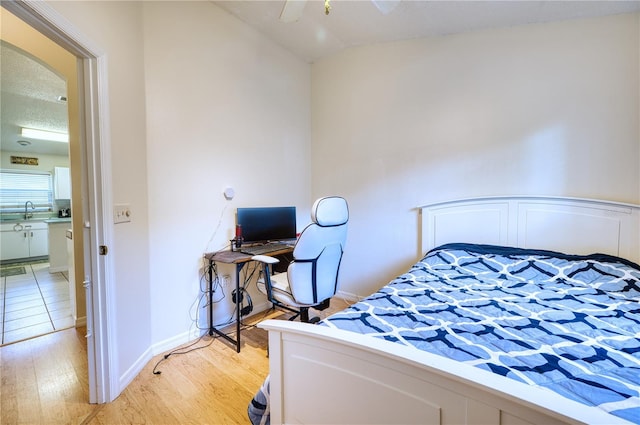 bedroom featuring sink, vaulted ceiling, light hardwood / wood-style floors, and a textured ceiling