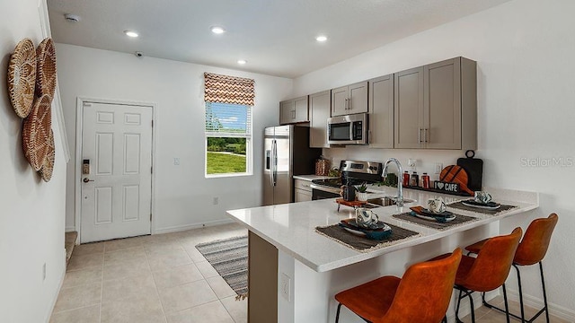 kitchen with stainless steel appliances, kitchen peninsula, a breakfast bar, and gray cabinets