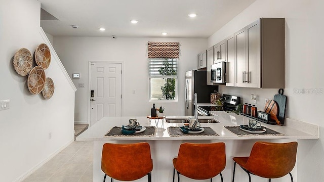 kitchen with stainless steel appliances, a kitchen breakfast bar, kitchen peninsula, light tile patterned flooring, and gray cabinetry