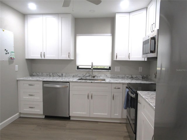 kitchen with sink, light stone counters, wood-type flooring, stainless steel appliances, and white cabinets