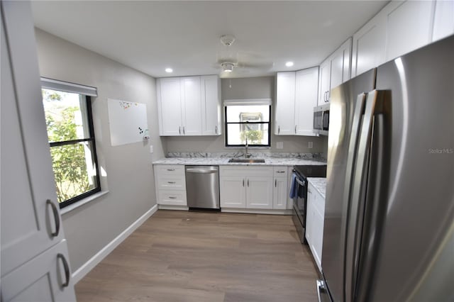 kitchen featuring appliances with stainless steel finishes, sink, white cabinets, light hardwood / wood-style floors, and light stone countertops