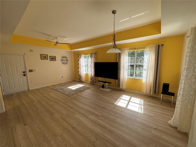 unfurnished living room with ceiling fan, light hardwood / wood-style floors, and a tray ceiling