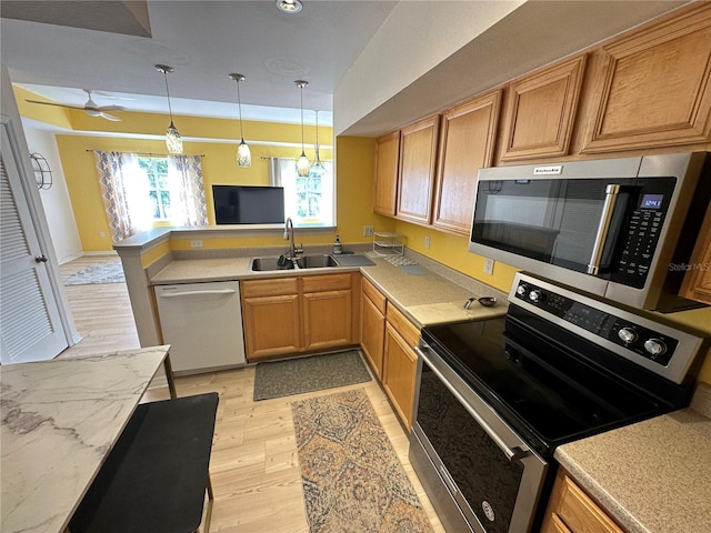 kitchen featuring kitchen peninsula, hanging light fixtures, sink, light hardwood / wood-style floors, and stainless steel appliances