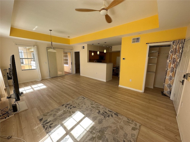 unfurnished living room featuring ceiling fan, a raised ceiling, and light hardwood / wood-style flooring