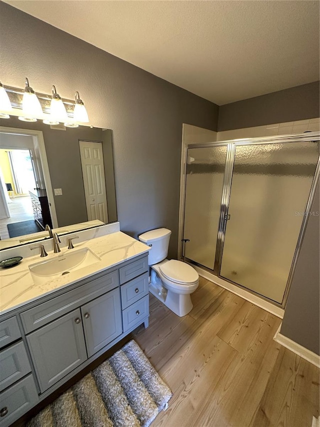 bathroom featuring hardwood / wood-style floors, a shower with door, toilet, and vanity