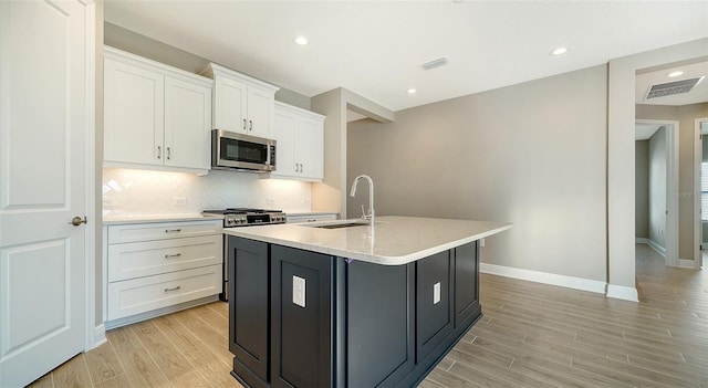 kitchen featuring backsplash, a kitchen island with sink, light stone countertops, white cabinets, and sink