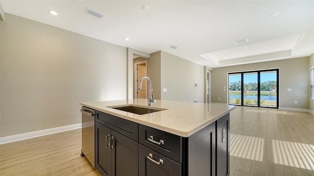 kitchen with dishwasher, a center island with sink, a raised ceiling, sink, and light stone countertops