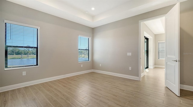 unfurnished room featuring a raised ceiling and light hardwood / wood-style flooring