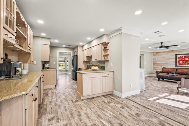 kitchen featuring light brown cabinetry, light stone counters, light hardwood / wood-style flooring, black refrigerator, and wooden walls