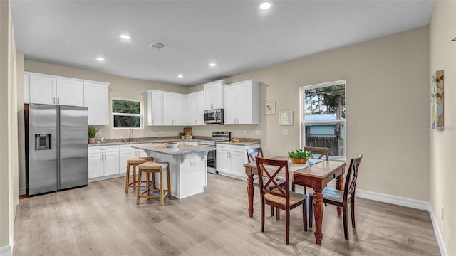 kitchen with white cabinetry, a breakfast bar, a center island, and appliances with stainless steel finishes