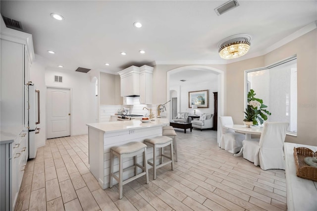 kitchen featuring white cabinetry, backsplash, a kitchen bar, light hardwood / wood-style floors, and kitchen peninsula