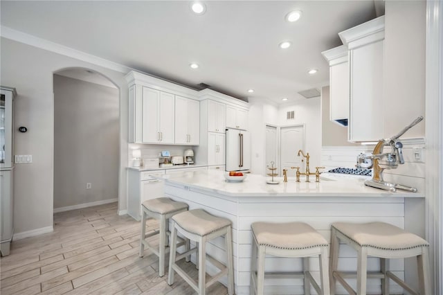 kitchen with a breakfast bar, sink, white cabinetry, high end refrigerator, and light hardwood / wood-style floors