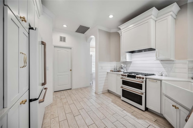 kitchen with white cabinetry, tasteful backsplash, light wood-type flooring, white refrigerator, and range with two ovens