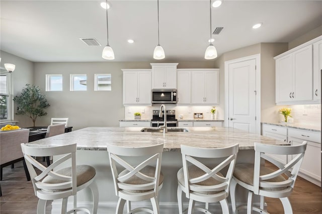 kitchen with sink, backsplash, hanging light fixtures, a kitchen island with sink, and stainless steel appliances