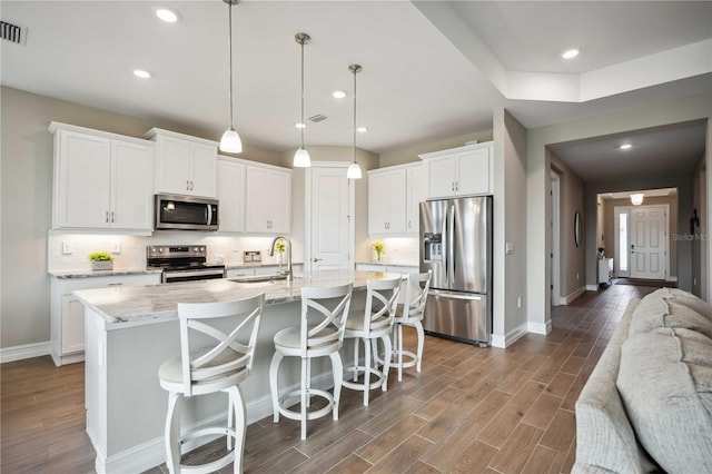 kitchen featuring appliances with stainless steel finishes, pendant lighting, white cabinetry, sink, and a center island with sink