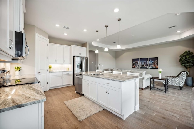 kitchen with sink, a kitchen island with sink, stainless steel appliances, white cabinets, and decorative light fixtures