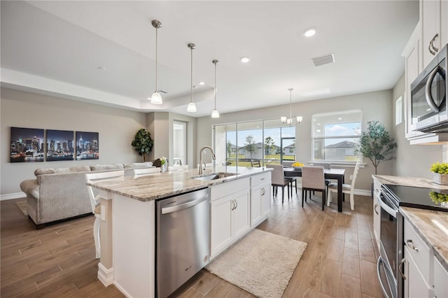 kitchen with stainless steel appliances, a kitchen island with sink, sink, and white cabinets