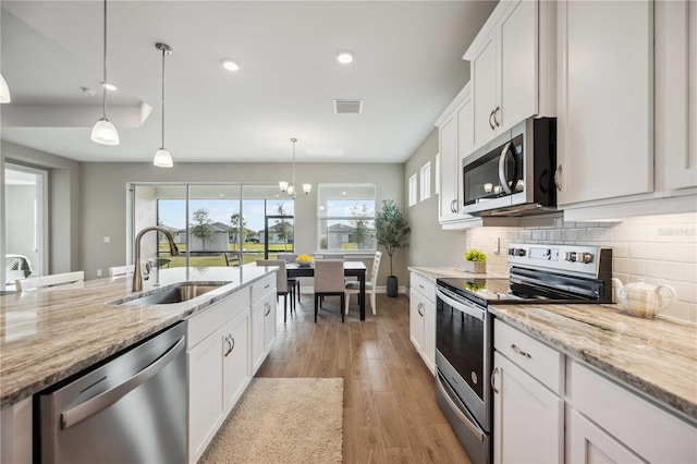 kitchen with sink, light stone counters, hanging light fixtures, appliances with stainless steel finishes, and white cabinets