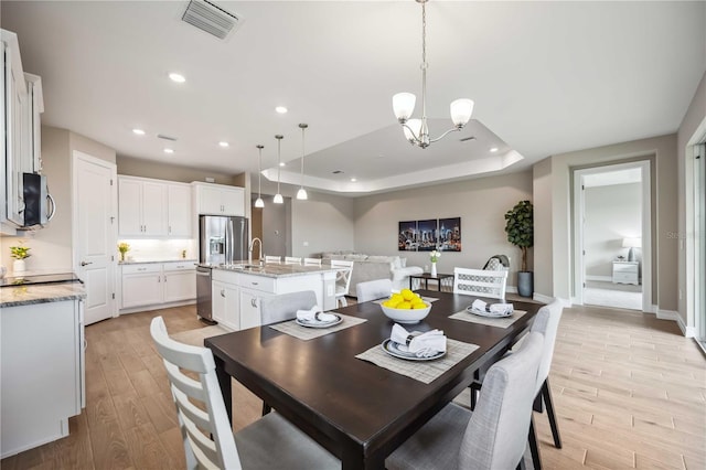 dining space featuring light hardwood / wood-style floors, a raised ceiling, sink, and a notable chandelier