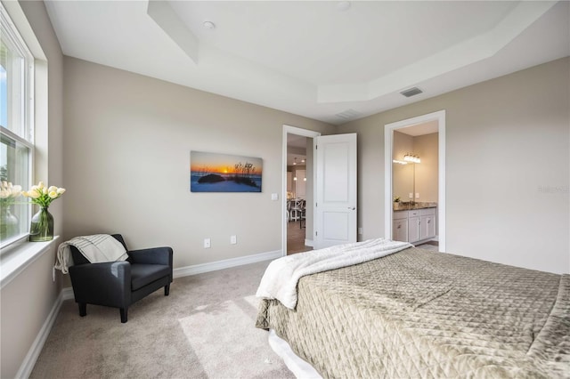 bedroom with ensuite bath, a raised ceiling, and carpet