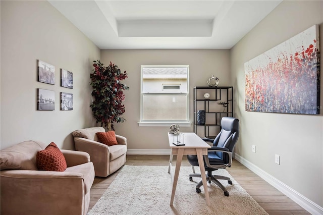 home office featuring a raised ceiling and light hardwood / wood-style flooring