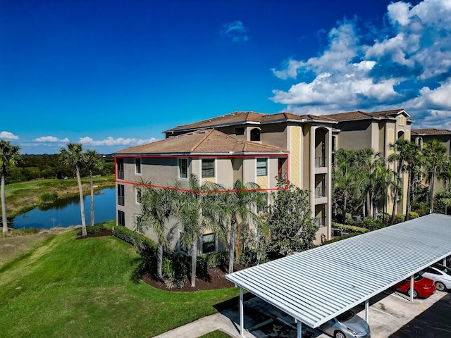 rear view of property featuring a carport, a water view, and a yard