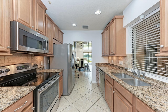 kitchen with sink, decorative backsplash, light tile patterned floors, stainless steel appliances, and light stone countertops