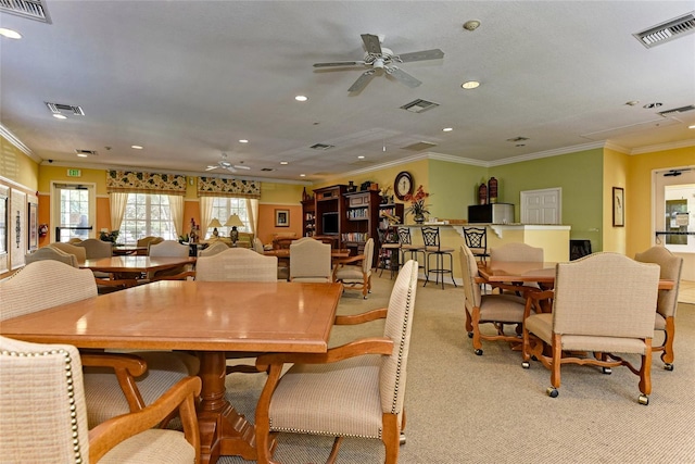 carpeted dining space with crown molding and ceiling fan