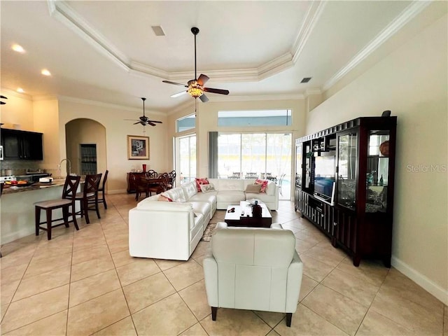 tiled living room featuring ceiling fan, a tray ceiling, and ornamental molding