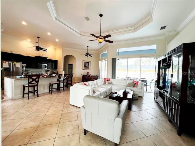 living room with a raised ceiling, ceiling fan, light tile patterned flooring, and ornamental molding