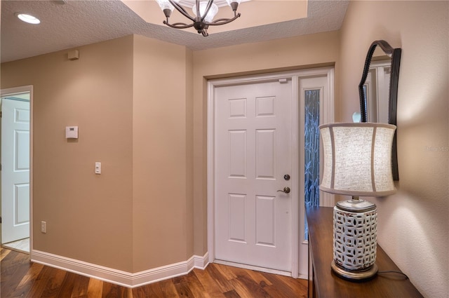 entrance foyer featuring dark wood-type flooring, a textured ceiling, and a notable chandelier