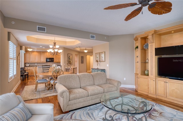 living room with a textured ceiling, ceiling fan with notable chandelier, light hardwood / wood-style flooring, and a tray ceiling