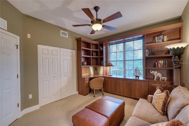 carpeted office space featuring ceiling fan, built in desk, and a textured ceiling