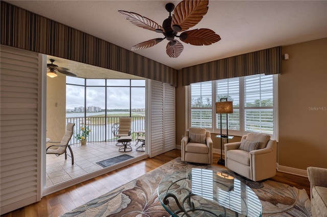 living room with a textured ceiling, a water view, light hardwood / wood-style flooring, and ceiling fan