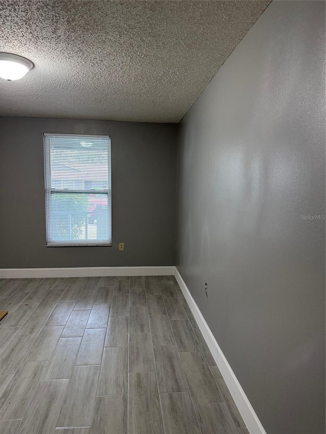 unfurnished room with light wood-type flooring and a textured ceiling