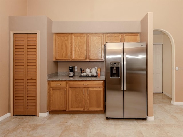 kitchen featuring light tile patterned floors, stainless steel fridge, and light stone counters