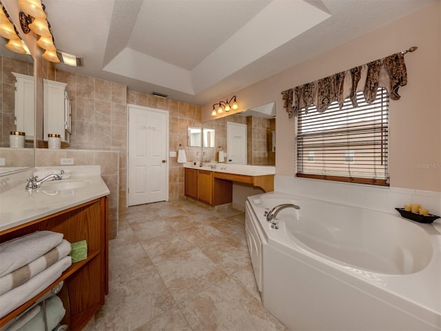 bathroom featuring a bath, tile walls, a tray ceiling, and vanity